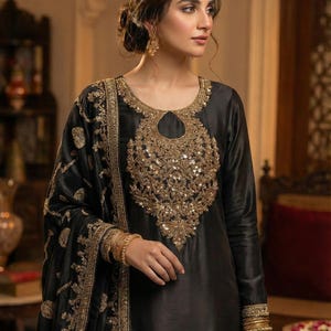 Pode incluir: Vestido de seda preto com bordados dourados. O vestido tem decote redondo e mangas compridas. O bordado dourado está concentrado no corpete e nas mangas. Inclui um xaile preto a condizer com detalhes dourados. A modelo usa pulseiras douradas.
