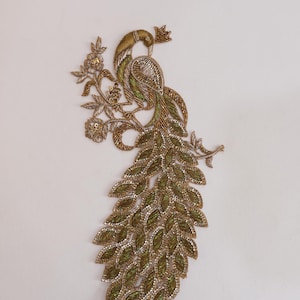 Puede incluir: Aplicación bordada de un pavo real coronado, posado en una rama florida. El pavo real presenta abalorios verdes, dorados y plateados, con una larga cola de hojas verde oliva. La aplicación es probablemente para embellecer ropa o accesorios.