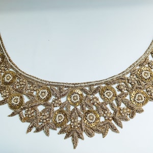 May include: Gold and white beaded neckline trim with a floral design. The trim is made of sequins, beads, and thread.