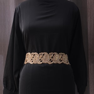 Może przedstawiać: Czarna sukienka z długimi rękawami i złotym, haftowanym paskiem. Pasek ma wzór paisley.