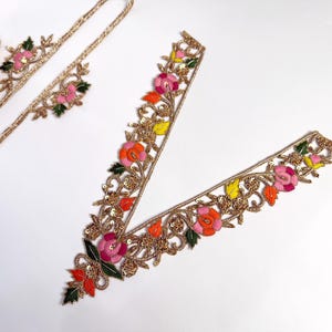 Puede incluir: Un ribete floral dorado con flores bordadas de colores. El ribete es perfecto para añadir un toque de elegancia a cualquier prenda.