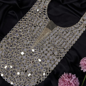 Puede incluir: Un adorno de espejo plateado y dorado en forma de lágrima. El adorno está hecho de pequeños espejos redondos cosidos sobre una base de tela.