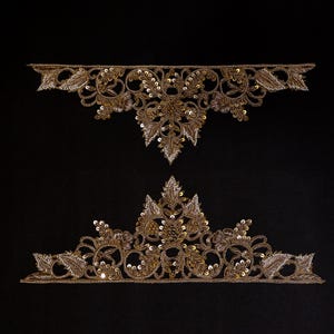 Può includere: Due applicazioni in pizzo dorato con intricati disegni floreali e a foglie. Le applicazioni sono impreziosite da paillettes e perline, su sfondo nero. L'applicazione superiore è curva, mentre quella inferiore ha la forma di una corona.