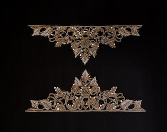 May include: Two ornate, gold-colored lace appliques with intricate floral and leaf designs. The appliques are embellished with sequins and beads, set against a black background. The top applique is a curved shape, and the bottom one is a crown shape.