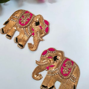 May include: Two gold embroidered elephant appliques with pink and black details. The elephants are decorated with sequins and pearls.