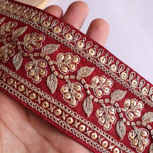 Può includere: Bordura ricamata color bordeaux con motivi floreali e a foglie dorate. La bordura presenta intricati dettagli di paillettes e filo dorato lungo i bordi e all'interno dei disegni floreali. Ideale per abbellire capi di abbigliamento o progetti artigianali.