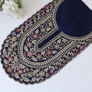 May include: A dark navy blue fabric neckline applique featuring intricate embroidery in shades of red, gold, and cream. The design includes floral motifs and leafy vines with a scalloped edge, accented by subtle metallic sequins throughout.