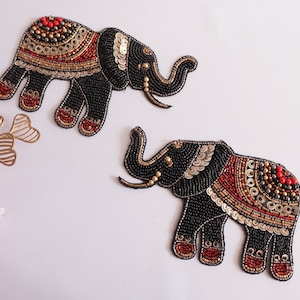 May include: Two beaded elephant patches. The elephants are black with red, gold, and silver accents. The patches are decorated with beads and sequins. The elephants have their trunks raised and are facing left.