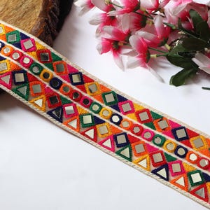 Peut inclure: Une garniture décorative colorée avec des motifs géométriques et des accents miroir. La garniture présente des carrés, des triangles et des cercles dans des teintes vives d'orange, de rose, de vert et de jaune. Idéal pour les projets créatifs.