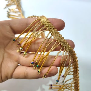 May include: Gold beaded fringe trim with iridescent beads. The fringe is made of small gold beads strung on thin gold wires.