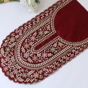 Könnte beinhalten: Ein tiefrotes Stoff-Halsstück mit aufwendiger Blumenstickerei in Rosa-, Gold- und Grüntönen. Das Design umfasst Paillettenakzente und einen gewellten Rand mit einer dekorativen Bordüre, die eine detaillierte Verzierung für Kleidungsstücke bildet.