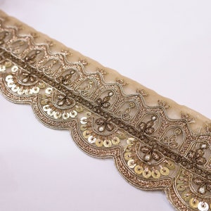 May include: Gold and brown embroidered trim with sequins. The trim has a scalloped edge and a delicate floral design.