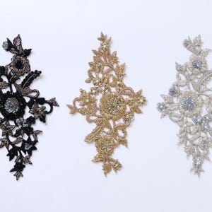 May include: Three decorative floral appliqués in black, gold, and silver. Each piece features intricate beadwork, sequins, and embroidery in a symmetrical botanical pattern with central flower motifs and surrounding leaves on a mesh base.