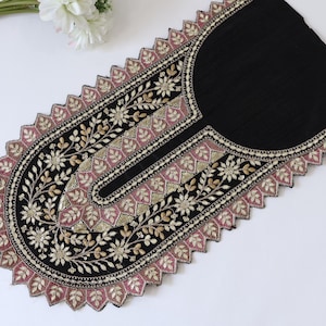 May include: A black fabric neckline applique featuring intricate embroidery in gold and pink thread. The design includes floral motifs and leaf patterns accented with small sequins. The edges are finished with a scalloped, zigzag border.