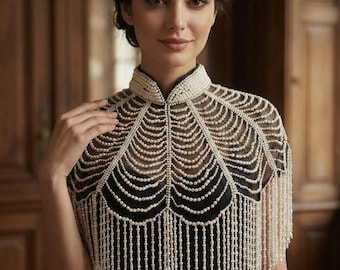 May include: A pearl beaded capelet with a high collar and fringe detailing. The capelet is made of small, round, off-white pearls and is worn over a black dress. The design is elegant and suitable for formal events.