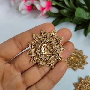 Könnte beinhalten: Goldene, blumenförmige Verzierung mit Pailletten und einem Perlenmittelpunkt. Die Verzierung hat einen Durchmesser von etwa 7,5 cm.