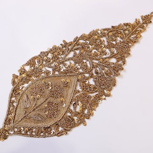 May include: Gold embroidered applique featuring a leaf design and intricate floral details. The applique is made with sequins and beads.