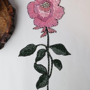 Könnte beinhalten: Eine rosa Rose mit grünen Blättern, beide aus Pailletten gefertigt. Die Rose hat eine perlmuttartige Mitte.