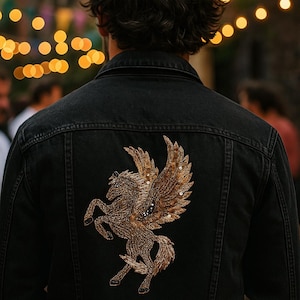May include: Black denim jacket with a detailed gold sequined Pegasus design on the back. The jacket has a classic denim style with visible stitching and a button-up front. The Pegasus is a mythical winged horse.
