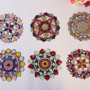 May include: Six circular embroidered patches with detailed sequin and bead patterns. Each patch displays a unique floral or geometric design in pink, blue, red, and gold. The patches are arranged on a white surface.