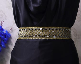 May include: A black dress with a decorative belt. The belt is gold and silver with a geometric pattern of mirrored triangles and squares. The belt is approximately 2 inches wide.