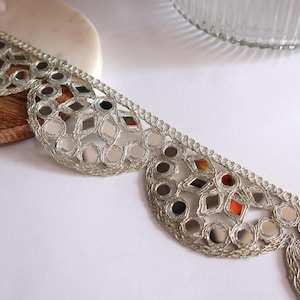 May include: Silver trim with a scalloped edge and mirrored embellishments. The trim is made of a delicate fabric with a metallic sheen.