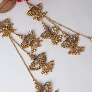Könnte beinhalten: Goldfarbene Dekorverzierungen mit einem mehrschichtigen Design, das mehrere kleine, goldfarbene, fächerförmige Teile mit Pailletten und Perlen aufweist.