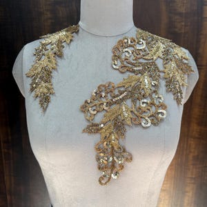 Peut inclure: Applique dorée à paillettes et perles avec un motif floral et de feuilles. L'applique est présentée sur un mannequin blanc.