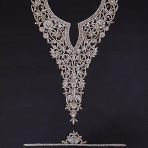 Peut inclure: Un col brodé argenté orné et une garniture assortie, avec des motifs floraux et de volutes complexes. Les ornements sont posés sur un fond sombre, soulignant le savoir-faire détaillé. La garniture est composée de deux lignes parallèles avec un motif floral.