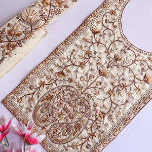 May include: A white embroidered fabric trim with a paisley design and floral motifs in brown and gold. The trim is perfect for adding a touch of elegance to any project.
