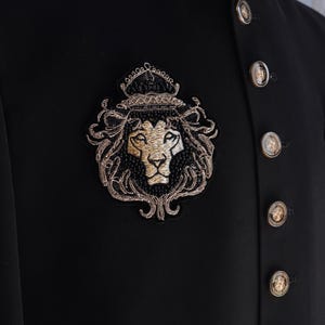 May include: A black blazer with gold embroidery featuring a lion head with a crown. The blazer has multiple gold buttons down the front.