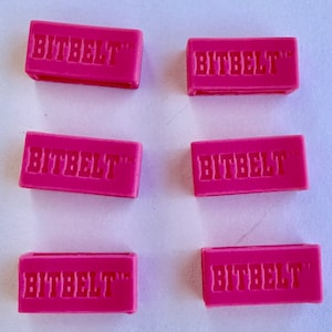 May include: Six pink plastic belt buckles with the text "BITBELT™" embossed on each.