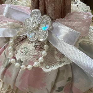 May include: A pink and white fabric pumpkin with a white lace trim, a white satin ribbon with a pearl and lace flower embellishment, and a pearl necklace.