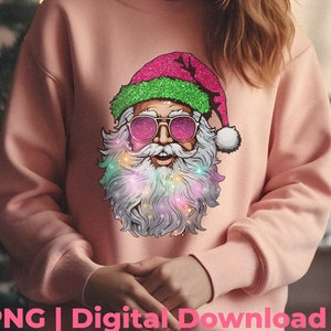 Op de afbeelding: Een lichtroze sweatshirt met een afbeelding van de kerstman met een zonnebril en een roze en groene glitterhoed. De kerstman heeft een witte baard met kleurrijke lichtjes. De tekst "PNG | Digital Download" is zichtbaar.