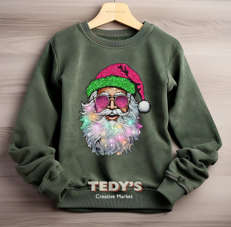 Op de afbeelding: Een olijfgroene sweatshirt met een afbeelding van de kerstman met een zonnebril en een roze glitterhoed. Zijn baard is versierd met kleurrijke lichtjes. De tekst "TEDY'S Creative Market" staat onderaan op de sweatshirt.