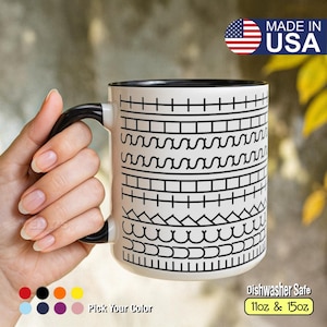 May include: White ceramic mug with a black handle and rim, featuring a repeating black geometric pattern. The mug is labeled "Made in USA" and "dishwasher safe", available in 11oz and 15oz sizes. The text "Pick Your Color" is also visible.