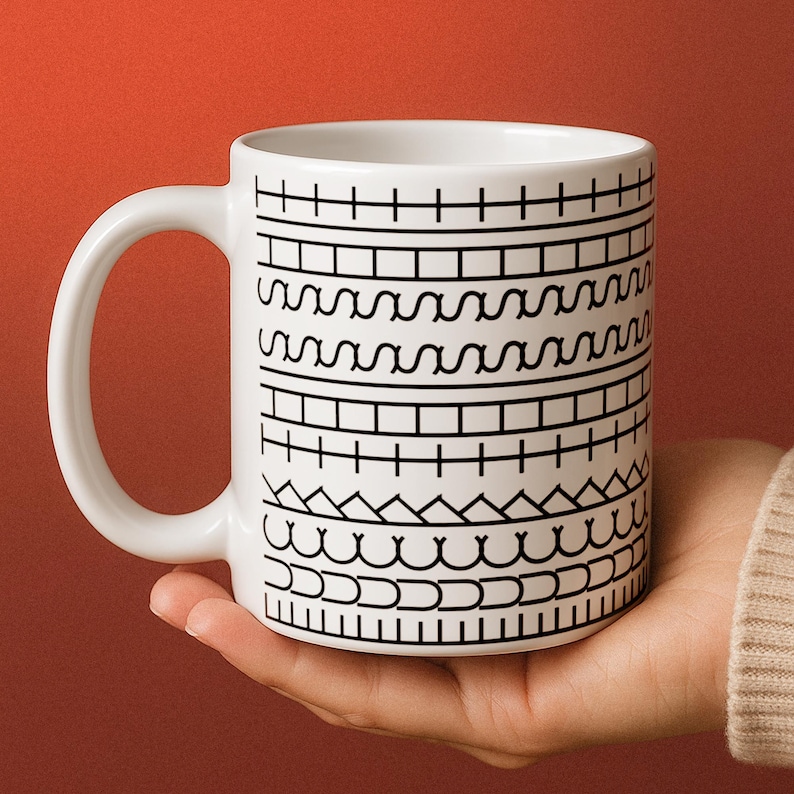 May include: White ceramic mug with a black geometric pattern. The mug has a curved handle and is held against a reddish-orange background. The pattern consists of various horizontal lines and shapes.