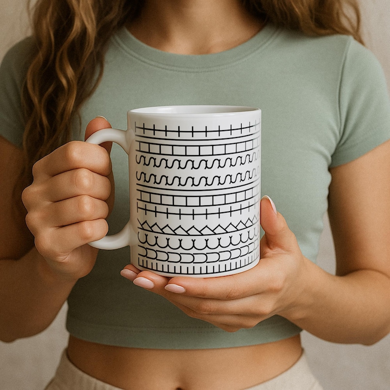 May include: White ceramic mug with a black geometric pattern. The mug features a series of horizontal bands with different black line designs. The mug has a white handle and is held by a person wearing a green shirt.