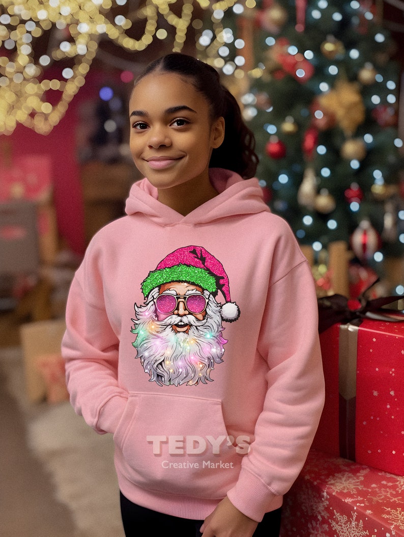 Op de afbeelding: Een lichtroze hoodie met een afbeelding van de kerstman met een zonnebril en een kleurrijke baard. De afbeelding van de kerstman staat op de voorkant. De hoodie heeft een voorzak en de tekst "TEDY'S Creative Market" is eronder gedrukt.
