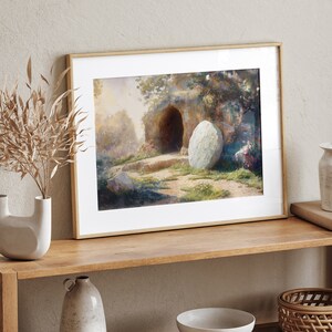 May include: A framed watercolor painting depicting a stone tomb with a large, round stone rolled away from the entrance. The scene is set in a lush, green landscape with trees and flowers.