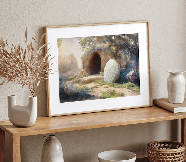 May include: A framed watercolor painting depicting a stone tomb with a large, round stone rolled away from the entrance. The scene is set in a lush, green landscape with trees and flowers.