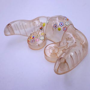 May include: A clear plastic lobster figurine with colourful flower and heart stickers. The lobster is in a curled position with its claws raised.