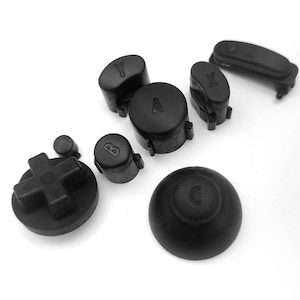 May include: A set of black replacement buttons for a video game controller. The buttons are labeled A, B, X, Y, and have a directional pad.