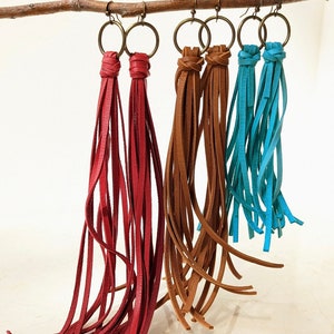 May include: Three pairs of leather tassel earrings. One pair is red, one pair is brown, and one pair is turquoise.