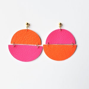 Puede incluir: Un par de pendientes de cuero de color rosa brillante y naranja con un diseño geométrico de medio círculo.