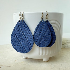 May include: A pair of navy blue teardrop earrings with a textured, woven pattern. The earrings hang from antique brass-colored ear wires. The earrings are displayed in a white ceramic pot.