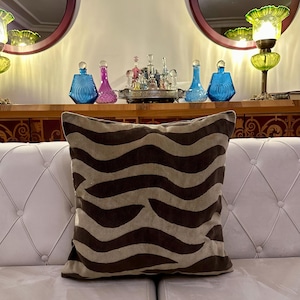 May include: A brown and beige striped throw pillow with a wave pattern. The pillow is on a white couch with tufted buttons.