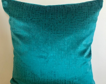 Puede incluir: Una almohada de tiro azul turquesa con un tejido tejido texturizado. La almohada es de forma cuadrada y tiene un brillo sutil.