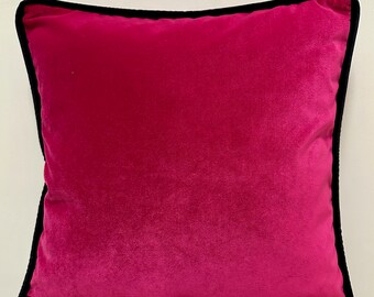 May include: A bright pink square pillow with a black border. The pillow is made of a soft, velvety fabric.