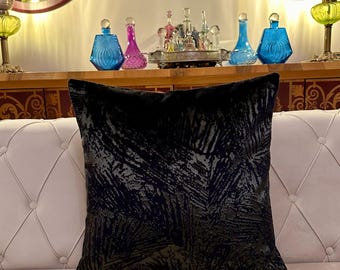 May include: A black throw pillow with a gold leaf pattern on a white couch. The pillow is in focus and the couch is out of focus.